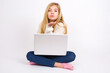 © Jihan - caucasian teen girl sitting with laptop in lotus position on white background looking at the camera blowing a kiss with hand on air being lovely. Love expression.