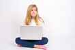 © Jihan - Amazed puzzled caucasian teen girl sitting with laptop in lotus position on white background , curves lips and has worried look, sees something awful in front.