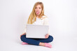 © Jihan - Body language. Disgusted stressed out caucasian teen girl sitting with laptop in lotus position on white background , frowning face, demonstrating aversion to something.