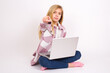 © Jihan - Cheerful caucasian teen girl sitting with laptop in lotus position on white background indicates happily at you, chooses to compete, has positive expression, makes choice.