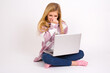© Jihan - caucasian teen girl sitting with laptop in lotus position on white background , holding his nose because of a bad smell.