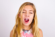Little Caucasian Kid Girl Wearing Sport Clothing Over White Background Yawns With Opened Mouth Stands. Daily Morning Routine