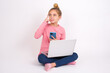 © Jihan - Beautiful caucasian teen girl sitting with laptop in lotus position on white background holding gadget while sticking out tongue
