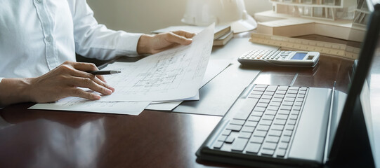 Engineers discuss a blueprint while checking information on a tablet computer in a office.