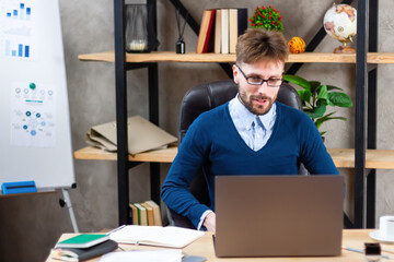 Smiling young confident successful businessman in eyeglasses, formal wear working on online project on laptop in modern office, communicating distantly with client, typing email, do electronic report