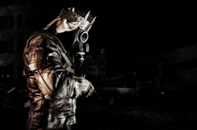 Photo Of Post Apocalyptic Warrior With Armored Outfit Jacket And Scrap Crown Standing Side View With Rifle On Dark Destroyed City Background.
