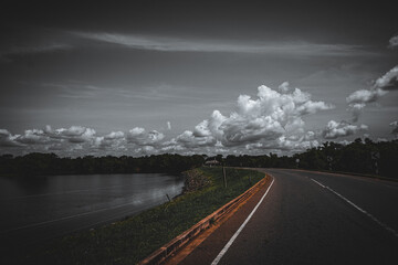 Poster - A scenic view of an empty road next to a green bank of a lake in monochrome colors