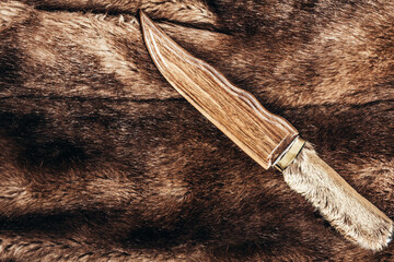 Photo of brown colored animal fur material with hunting knife with shleath laying on it.