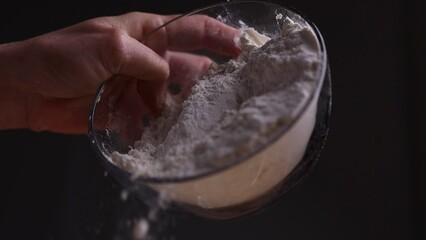 Poster - A slow motion of a hand pouring flour from glass plate on a black background