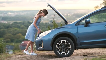 Wall Mural - Young woman driver standing near a broken car with open hood having trouble with her vehicle