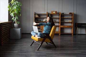 Wall Mural - Young relaxed woman freelancer in headset doing hands exercises at remote workplace, stretching arms while relaxing at comfortable cozy home office. Productivity home working during COVID-19 lockdown