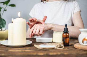 Wall Mural - Woman is smearing her hands with a natural organic cream doing a massage. Aroma lamp with essential oils and candles on the table. Concept of skin and self care in atmosphere of harmony and relaxation