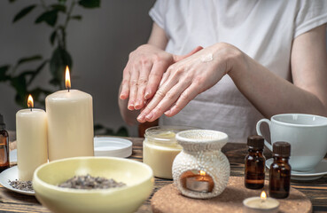 Wall Mural - Woman is smearing her hands with a natural organic cream doing a massage. Aroma lamp with essential oils and candles on the table. Concept of skin and self care in atmosphere of harmony and relaxation