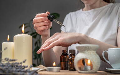 Wall Mural - Woman is smearing her hands with a natural organic oil. Aroma lamp with essential oils and candles on the table. Concept of skin and self care in atmosphere of harmony and relaxation