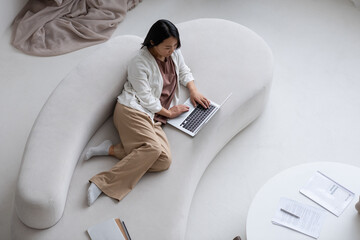 Aufkleber - Young serious female employee with laptop lying on sofa while networking, shopping online or working with financial data at home