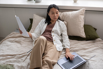 Aufkleber - Young serious female auditor concentrating on work with documents and online financial data on laptop screen while sitting on bed