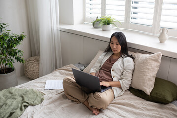 Aufkleber - Young serious businesswoman in casualwear typing on laptop keyboard while sitting on double bed in bedroom during work in home office