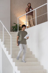 Aufkleber - Young serious businessman looking through document while going downstairs against Asian female employee talking on mobile phone