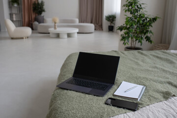 Aufkleber - Part of double bed with laptop, mobile phone and copybook with pen on background of interior of large living-room in modern apartment