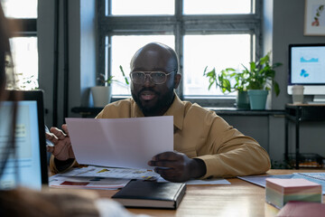 Aufkleber - Confident African-American economist with paper explaining financial data to colleague while sitting by table at working meeting