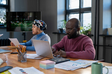 Aufkleber - Young serious economist in purple pullover typing on laptop keyboard while sitting by table and analyzing financial data in boardroom