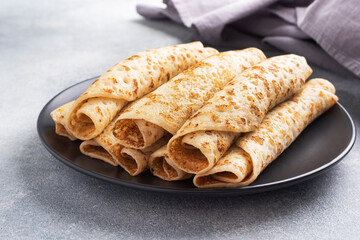 Thin pancakes rolled into a roll on a plate. The concept of a delicious breakfast or Maslenitsa. concrete background.