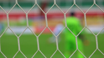 Wall Mural - soccer goalkeeper out of focus blurred in green uniform walks behind the net of soccer goal