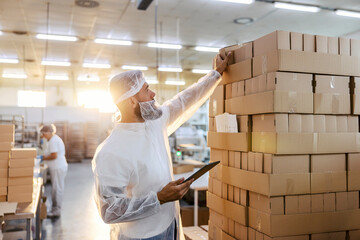 The food factory inspector in a white sterile uniform taking random boxes on from a pile. 