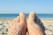 Two bare feet of caucasian woman soiled in sand with shell rock on sandy sea shore on sunny summer day close-up. Relaxing on sea sandy beach. Concept of rest, relaxation, vacation, travel tourism