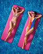 Beautiful young women floating on pink mattress in swimming pool
