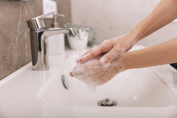 Wall Mural - Washing hands under the flowing water tap. Hygiene concept hand detail. Washing hands rubbing with soap for corona virus prevention, hygiene to stop spreading corona virus in or public wash room.