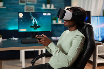 Canvas Print - Pro gamer woman wearing virtual reality googles holding gaming controller playing space shooter videogames during online competition. Concentrated gamer playing games using RBG computer equipment