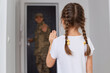 © sementsova321 - Indoor shot of military dad goes to war, little girl with dark hair and braids posing backwards and waving hand, saying good bye to father posing at the door.