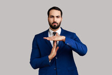Serious Strict Bearded Man Showing Time Out Gesture, Looking With Imploring Eyes, Hurry To Meet Deadline, Wearing Official Style Suit. Indoor Studio Shot Isolated On Gray Background.