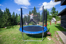 Happy Little Girl Jump On Trampoline In Backyard. Child Fun Outdoor. Summer Day. Blue Sky. Nature Landscape In Background.
