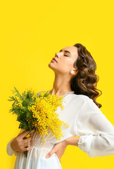 Wall Mural - Beautiful young woman with mimosa flowers on yellow background