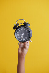  person hand holding alarm clock on yellow background ,