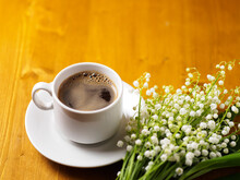 A White Cup Of Espresso Coffee And A Bouquet Of Lilies Of The Valley On A Wooden Table. Spring Time