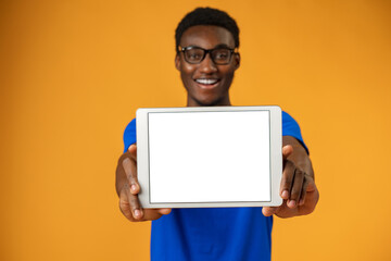 African american man showing blank digital tablet screen with copy space in yellow studio.