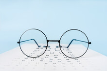A Table For Checking Vision In Russian, Glasses And Lenses On A Light Blue Background. A Concept For An Ophthalmology Clinic Or The Sale Of Optics