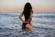 © alexkoral - young brunette girl with a sexy ass in a swimsuit is kneeling in the water in waves of sea near beach in summer on vacation