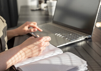 Poster - Woman hands taking notes in planner and working on laptop in cafe. Online education and work concept. Closeup. High quality photo