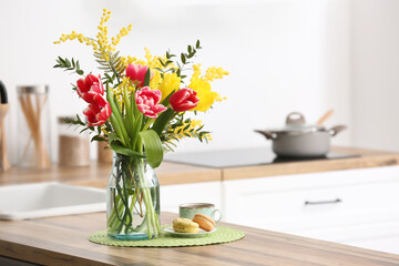 Vase with beautiful flowers, macarons and cup of coffee on kitchen counter