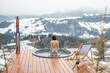 Woman standing in hot tub on terrace with great view on mountains during winter. Concept of rest and recovery in hot vat on nature. Idea of escape and recreation on mountains