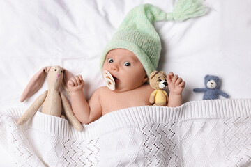 Sticker - Cute little baby with toys lying under knitted plaid in bed, top view