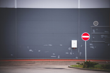 gray stripped industrial building wall, no entry road sign on green lawn isle, asphalt pavement