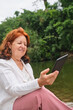 © Carolina Jaramillo - Mature hispanic woman reading an ebook on an electronic reader sitting in a park
