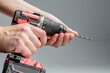 The man's hands install the drill into the drill, the hands take the drill and install it into the electric drill. Cordless tool on a gray background. DIY repair.