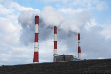 Thermal power plant with three pipes in the background and blue sky polluting the environment.