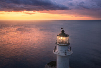 Wall Mural - lighthouse on the mountain peak at colorful sunset in summer. aerial view. beautiful lighthouse, lig